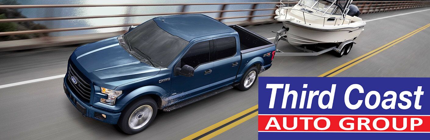 A blue Ford pick-up tows a boat on a trailer down a highway. Large text in the lower-right says, "Third Coast Auto Group."