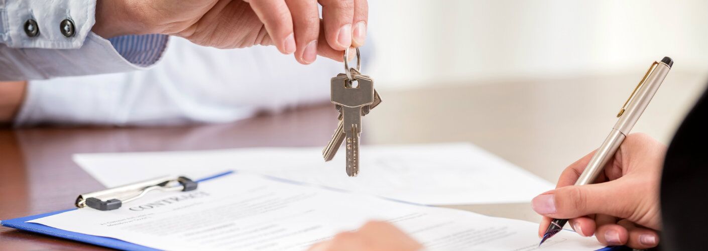 person signing documents while another person offers them keys