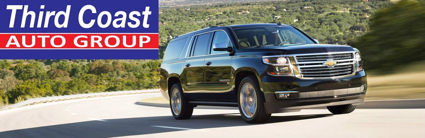 2017 Chevy Suburban driving on a curving road with the Third Coast Auto Group logo in the upper left corner of the image