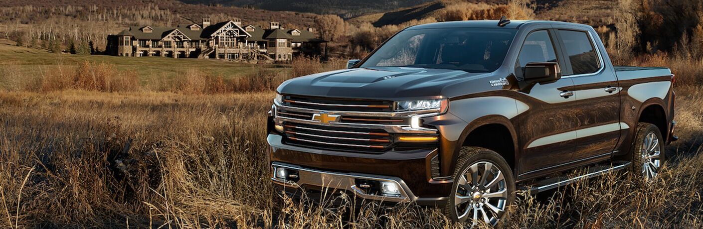 2019 Chevy Silverado parked in a field near a mountain lodge