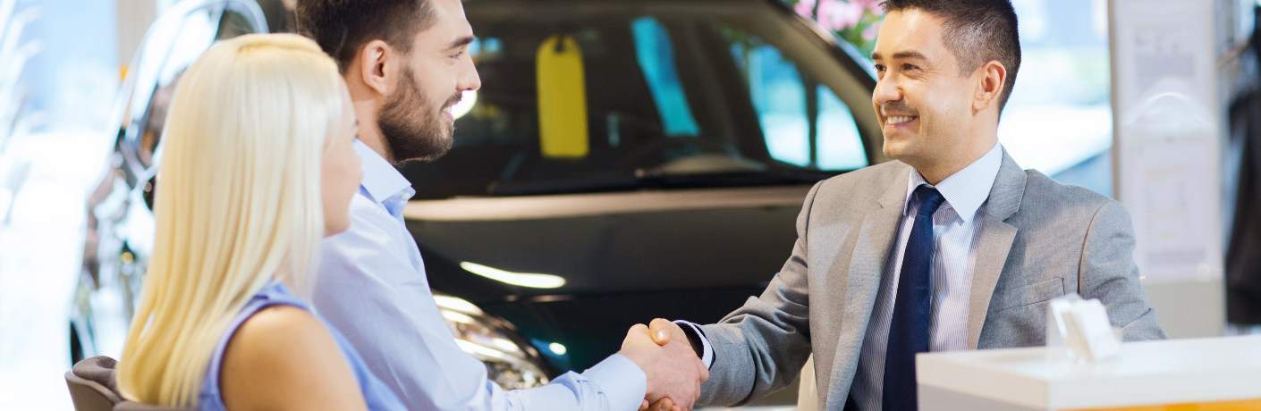 Couple shaking hands with a car salesman
