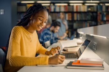 A black, female collelge student takes notes at the library