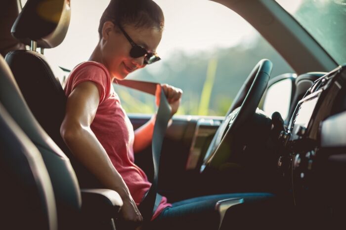 an asian woman wearing sunglasses smiles as she buckles her seatbelt