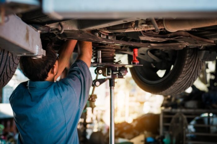 a mechanic in denim works on an elevated car
