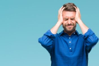 photo of a man in a blue shirt squeezing his eyes shit and grasping his head with both hands