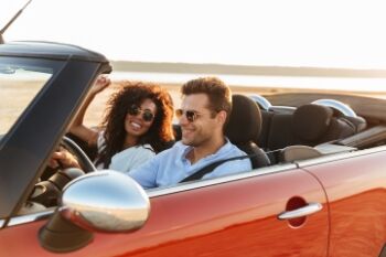 man and woman in sunglasses driving in a red convertible