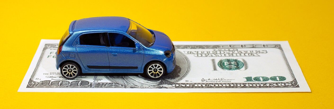 a tiny toy blue car parked on a hundred dollar bill symbolizes car credit