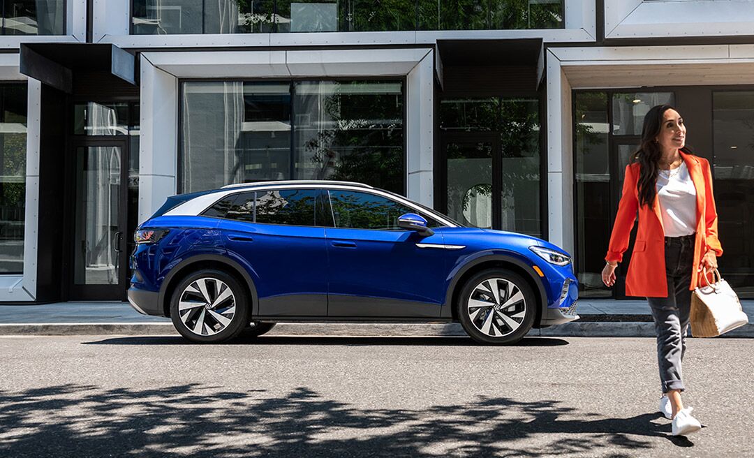 A woman walks away from an ID.4 in Dusk Blue Metallic that’s parked on an urban street.