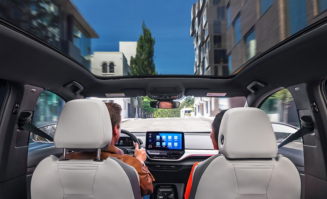 A forward facing shot of an ID.4 with focus on the driver and passenger seats, center console display, and available panoramic sunroof.