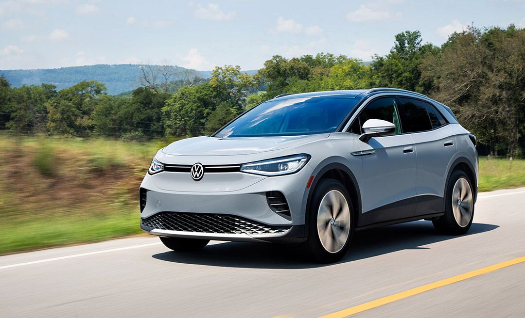 An ID.4 in Moonstone Gray drives along a highway with trees and mountains in the background.