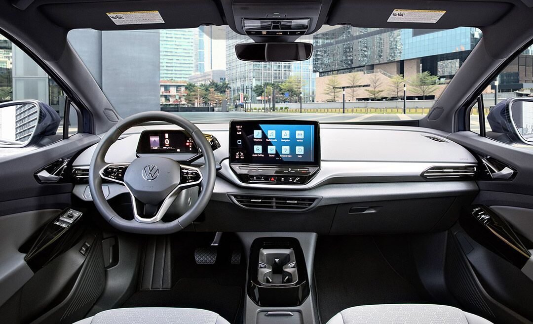 Interior shot of an ID.4 with focus on the front windshield, the dashboard, steering wheel, cup holder and center console display.