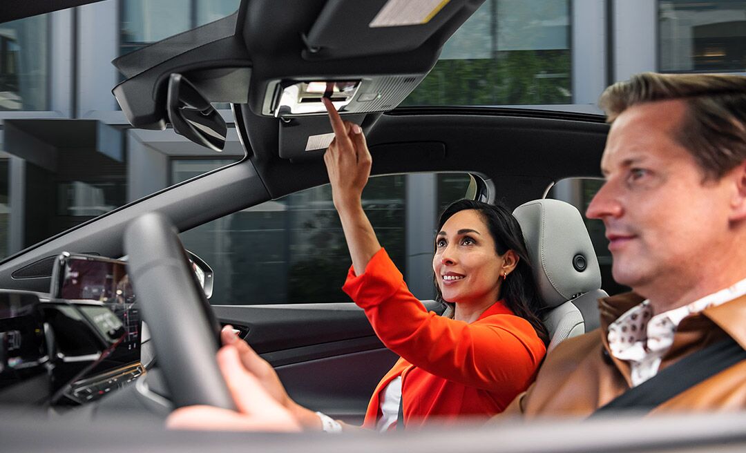 A man and woman sit in the front seats of an ID.4 while the woman in the passenger seat adjusts the controls for the sunshade.