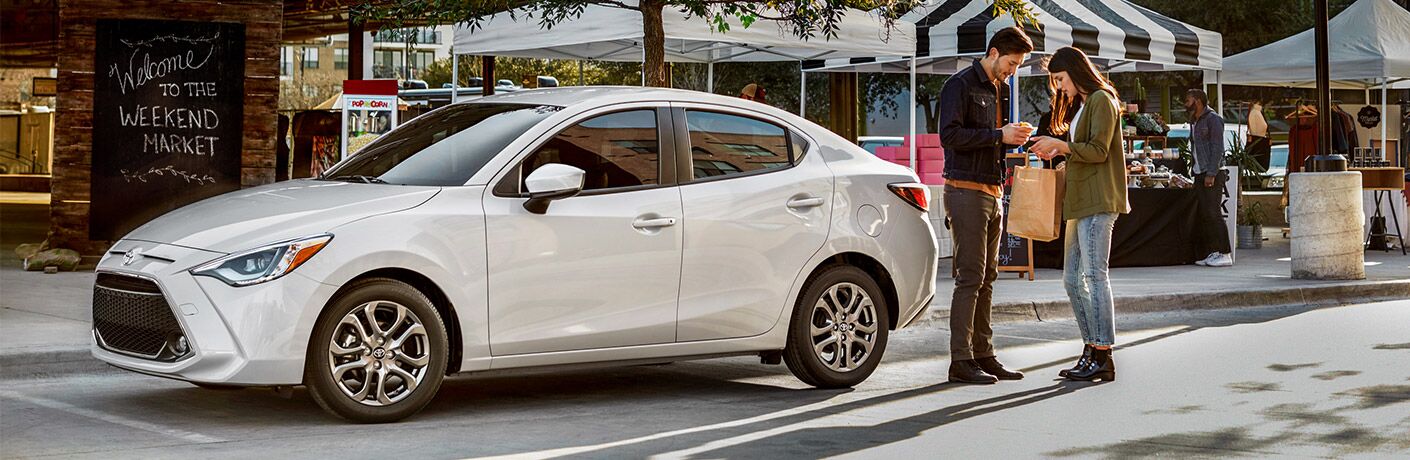 Man and woman standing next to white 2019 Toyota Yaris Sedan