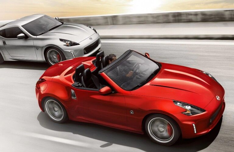 Front passenger angle of a red 2019 Nissan 370Z Roadster driving on a road with another 370Z Roadster driving behind it