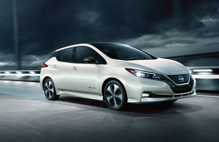 Front passenger angle of a white 2019 Nissan LEAF driving down a road at night