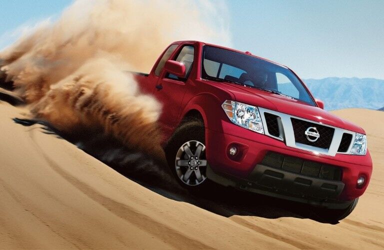 Front passenger angle of a red 2019 Nissan Frontier driving through heavy sand