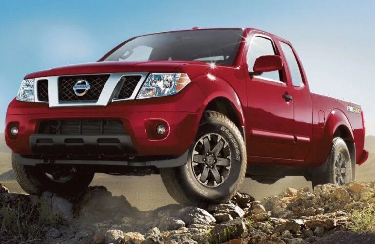 Front driver angle of a red 2019 Nissan Frontier with its front wheels resting on rocks