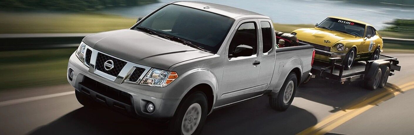 Front driver angle of a grey 2019 Nissan Frontier pulling a trailer with a yellow vehicle on top
