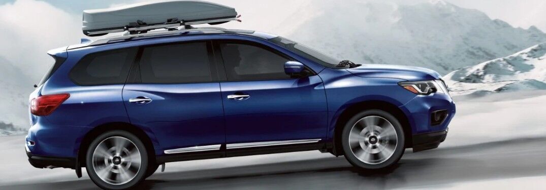 Passenger angle of a blue 2019 Nissan Pathfinder driving with snowy mountains in the background