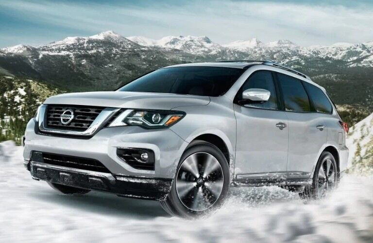 Front driver angle of a white 2019 Nissan Pathfinder driving through snow with mountains in the background