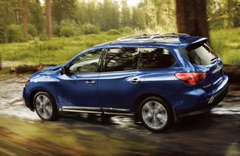 Rear driver angle of a blue 2019 Nissan Pathfinder driving through a shallow stream