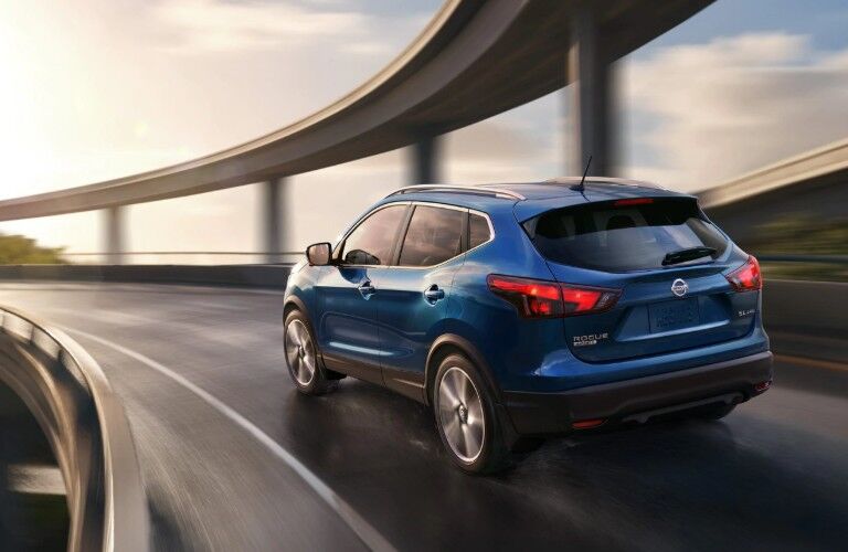 Rear driver angle of a blue 2019 Nissan Rogue Sport driving on a bridge