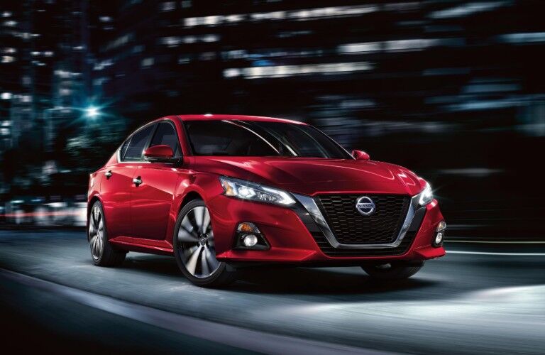 Front passenger angle of a red 2020 Nissan Altima driving at night through the city