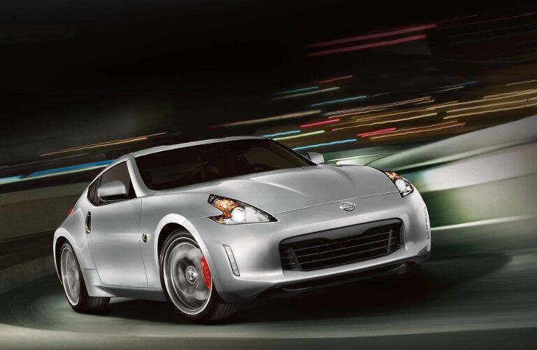 Front passenger angle of a silver 2020 Nissan 370Z driving down a road with a blurry background behind it