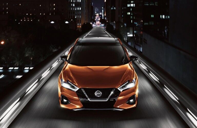 Front angle of an orange 2020 Nissan Maxima driving down a city street at night