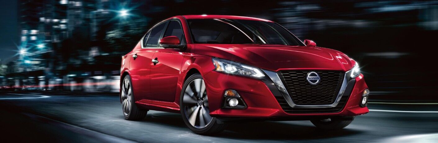 Front passenger angle of a red 2020 Nissan Altima driving at night through the city