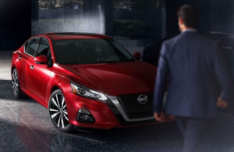 Front passenger angle of a red 2020 Nissan Altima with a man walking in front towards it