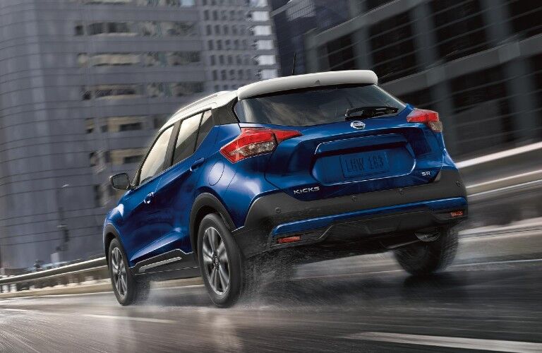 Rear driver angle of a blue 2020 Nissan Kicks with a white roof driving on a wet road