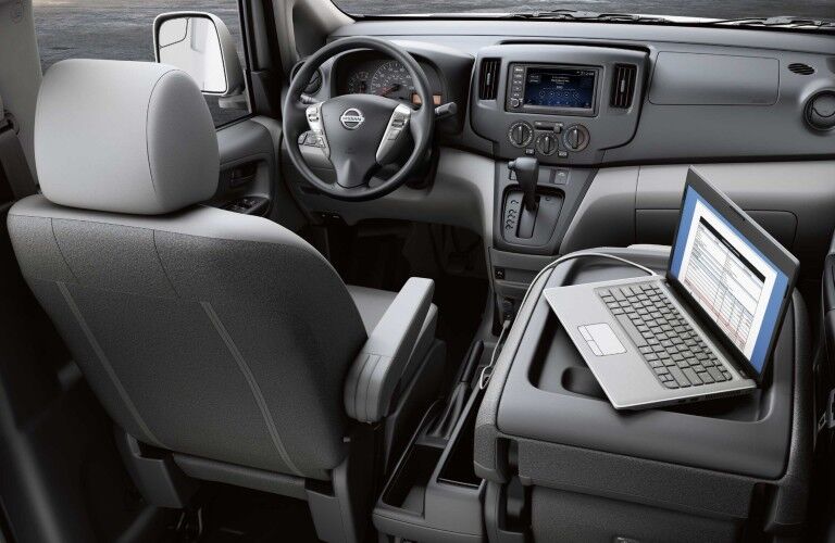 Front seats inside the 2020 Nissan NV200 Compact Cargo with the passenger seat folded and a laptop on top of it