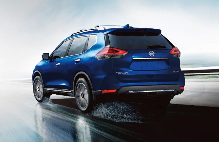 Rear driver angle of a blue 2020 Nissan Rogue driving on a wet road