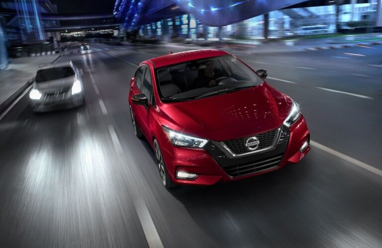Front passenger angle of a red 2020 Nissan Versa driving down a city road