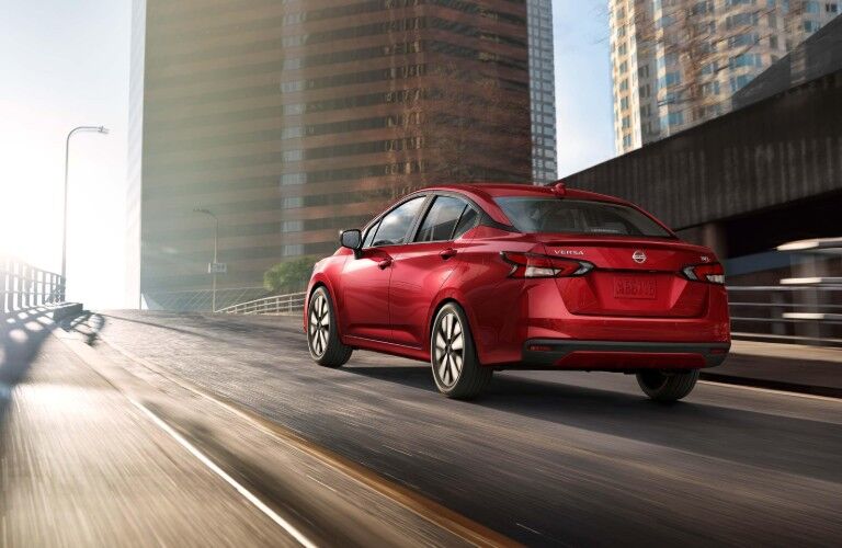 Rear driver angle of a red 2020 Nissan Versa driving down a city road