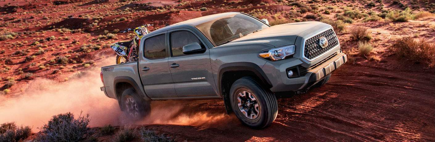 tan 2018 Toyota Tacoma carrying a motorbike driving up a dirty off-road hill