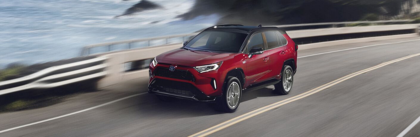 Red 2021 Toyota RAV4 Prime driving on a coastal road