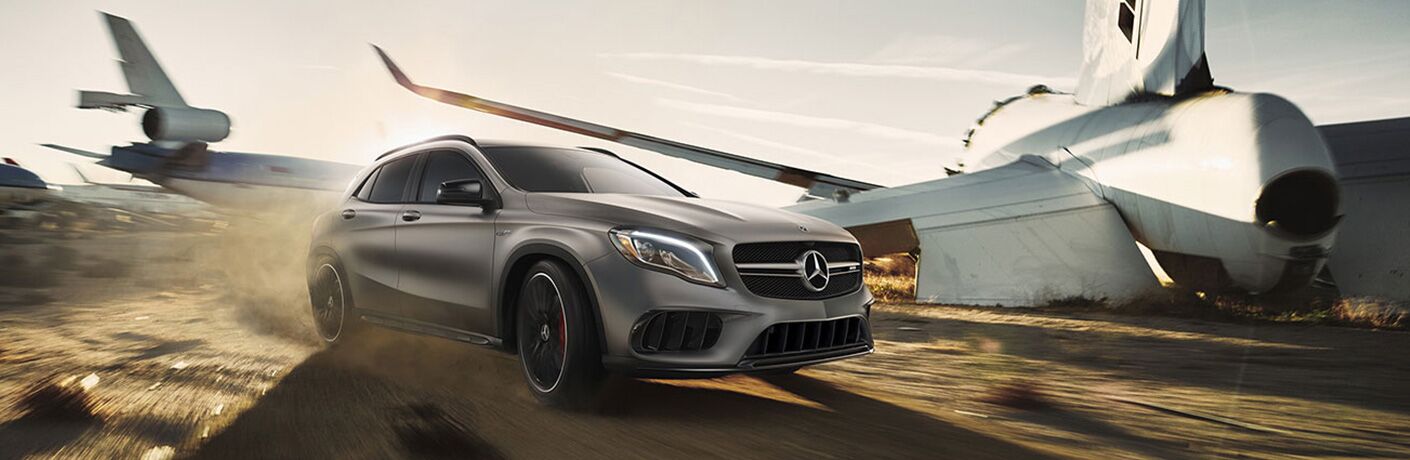 2019 MB AMG® GLA exterior front fascia and passenger side going fast on blurred dirt airfield with airplanes