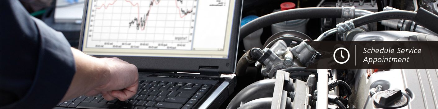 A mechanic typing on a computer on top of a car's engine