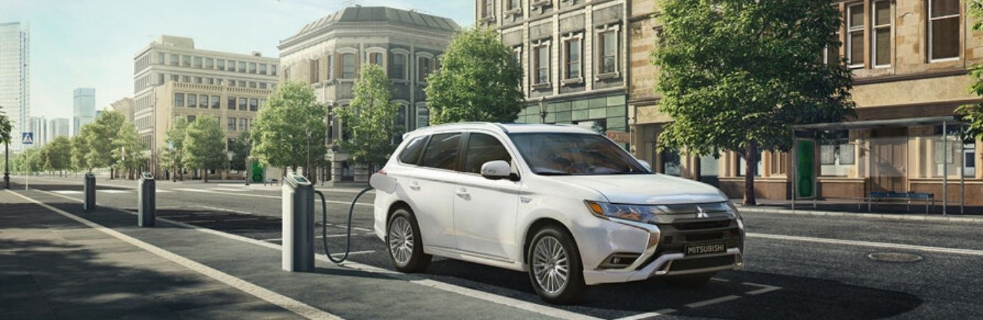 Image showing a white 2022 Mitsubishi Outlander PHEV charging at a public charging station on a city street