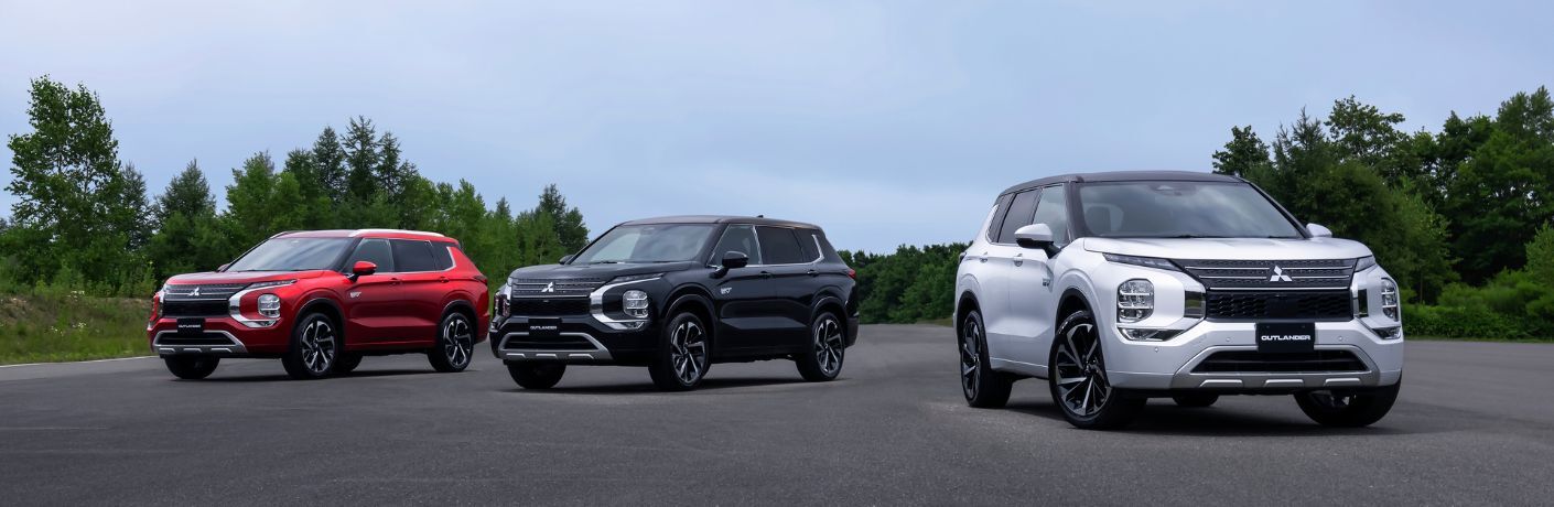 Image showing three 2023 Mitsubishi Outlander PHEV models in red, blue and white parked on a road.