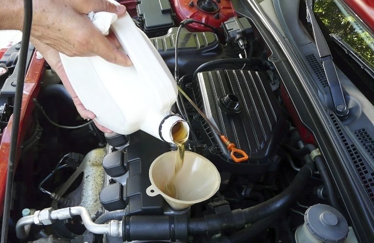 An auto mechanic adding oil with a funnel after a do-it-yourself oil change