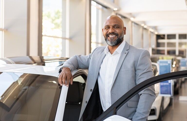 Happy car salesman standing by a white vehicle