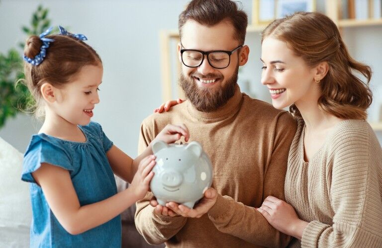Happy family helping daughter put money in a piggy bank