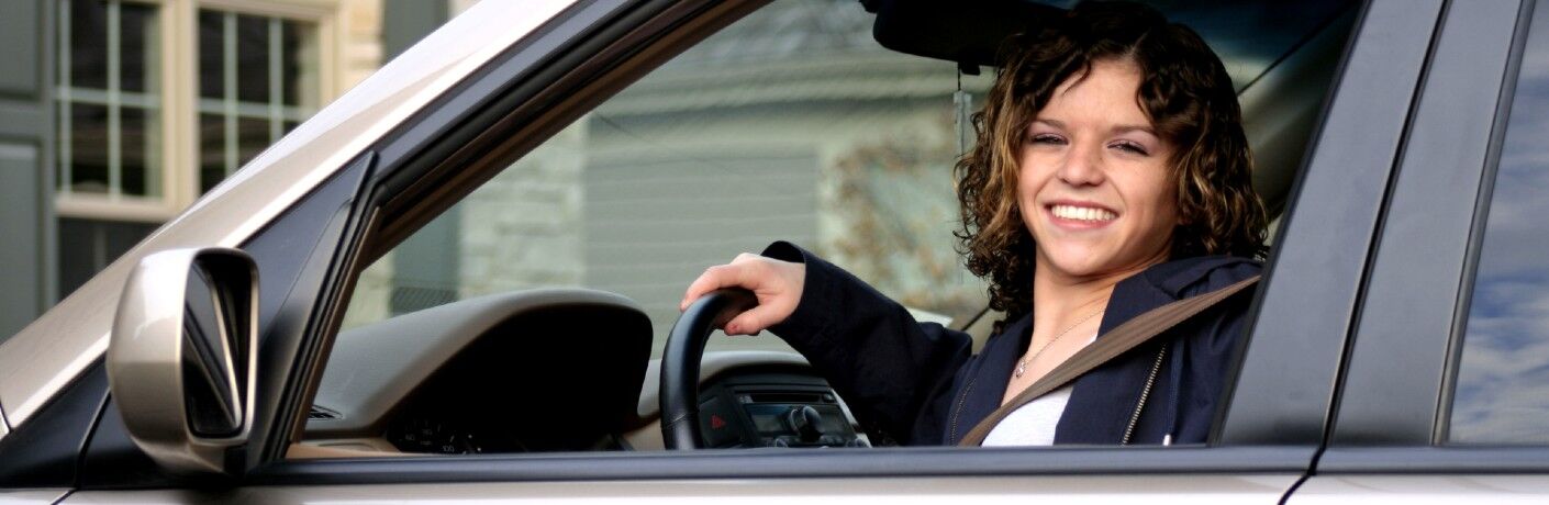 Happy young woman sitting in the driver's seat of a car