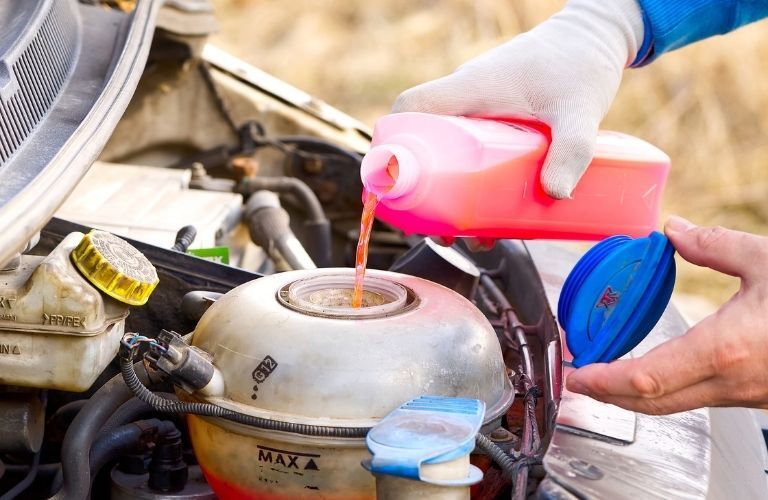 image of a technician's hand pouring fresh coolant in a car