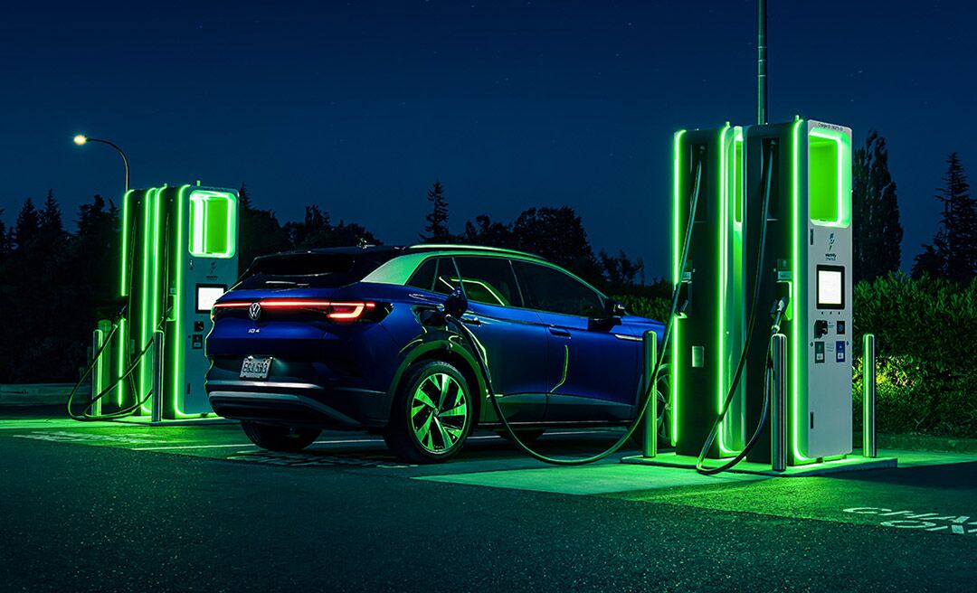 An ID.4 in Dusk Metallic Blue as it is parked at night next to a neon lit charging station.