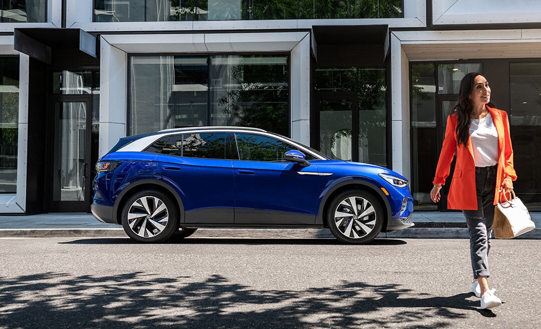A woman walks away from an ID.4 in Dusk Blue Metallic that’s parked on an urban street.