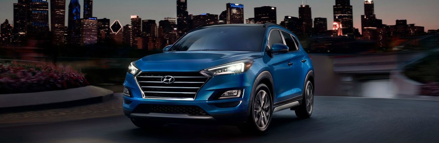 A blue-colored 2021 Hyundai Tucson parked with a city landscape in the background